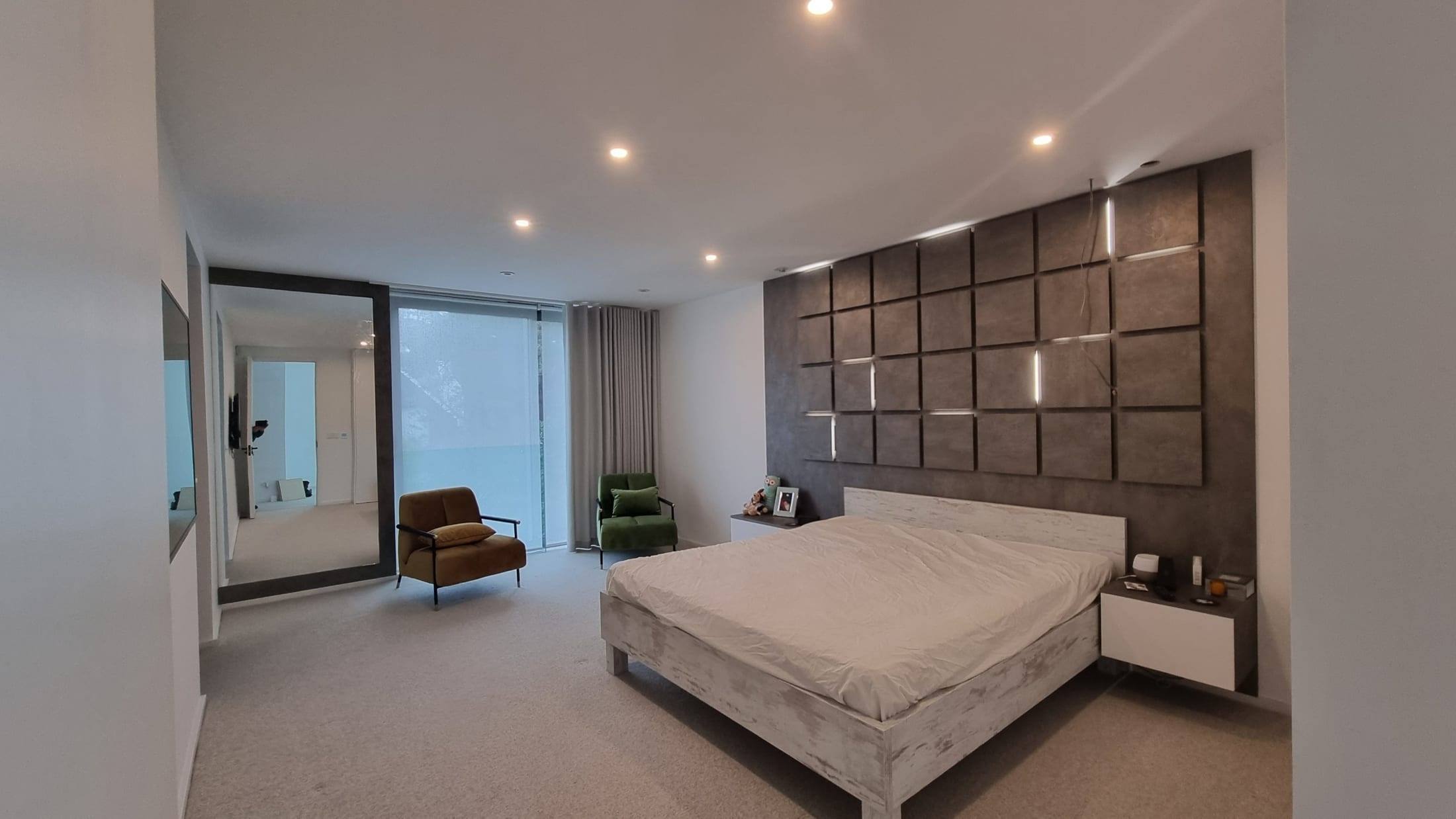 Contemporary bedroom with a panelled feature headboard wall, floating bedside units, bespoke bed and mirrored wardrobe door