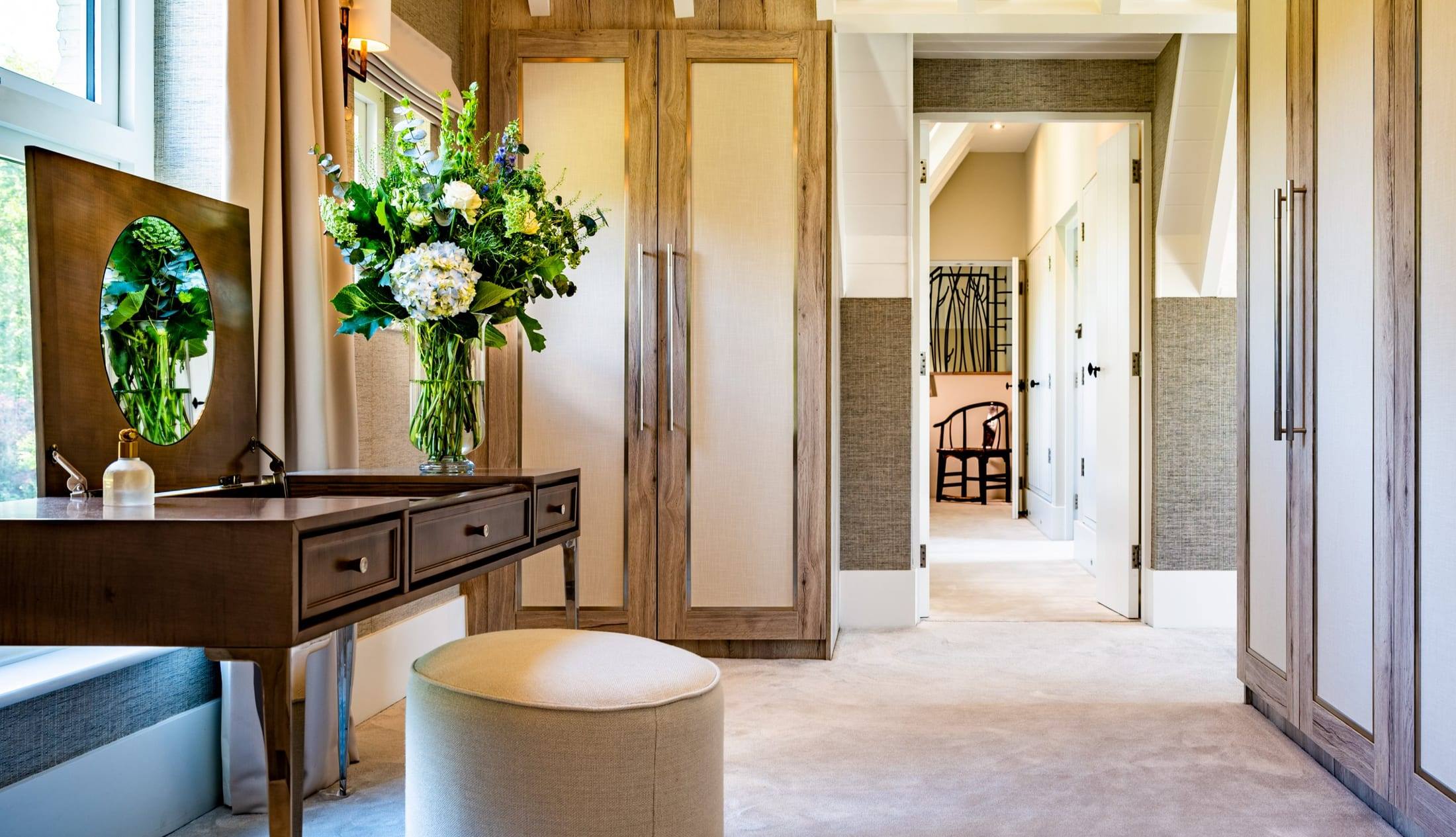 Dressing area with oak-effect fitted wardrobes with fabric panel doors and a bespoke dressing table
