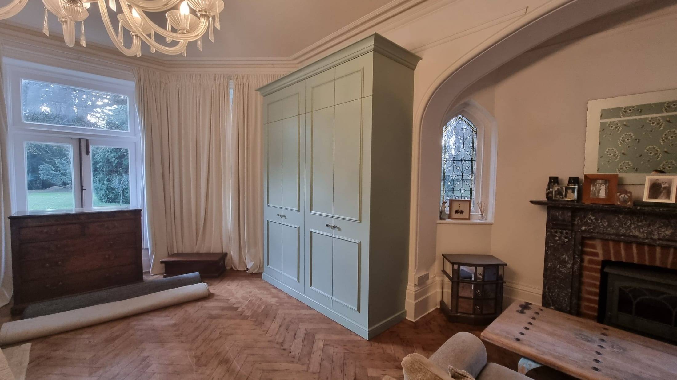 Bespoke fitted wardrobes with panelled doors, painted sage green and finished with cornice to suit a period bedroom