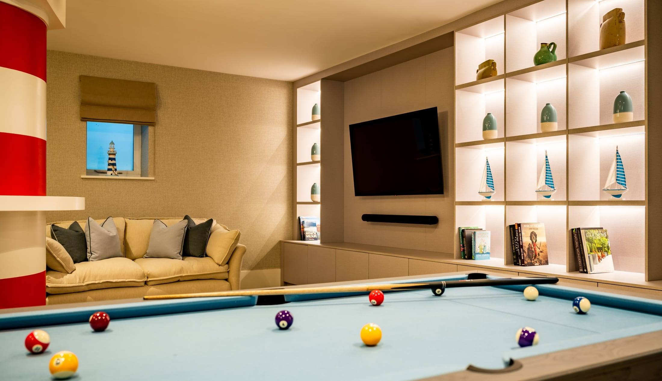 Games room with a fitted media wall, backlit display shelving and built-in storage drawers beside a pool table