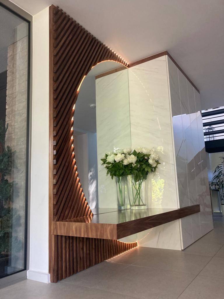 Entrance hall feature with curved walnut slat panelling, LED edge lighting and a floating walnut console shelf