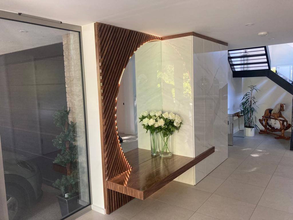 Wide view of a hallway with a curved walnut slat feature, floating console and tall marble-effect storage doors