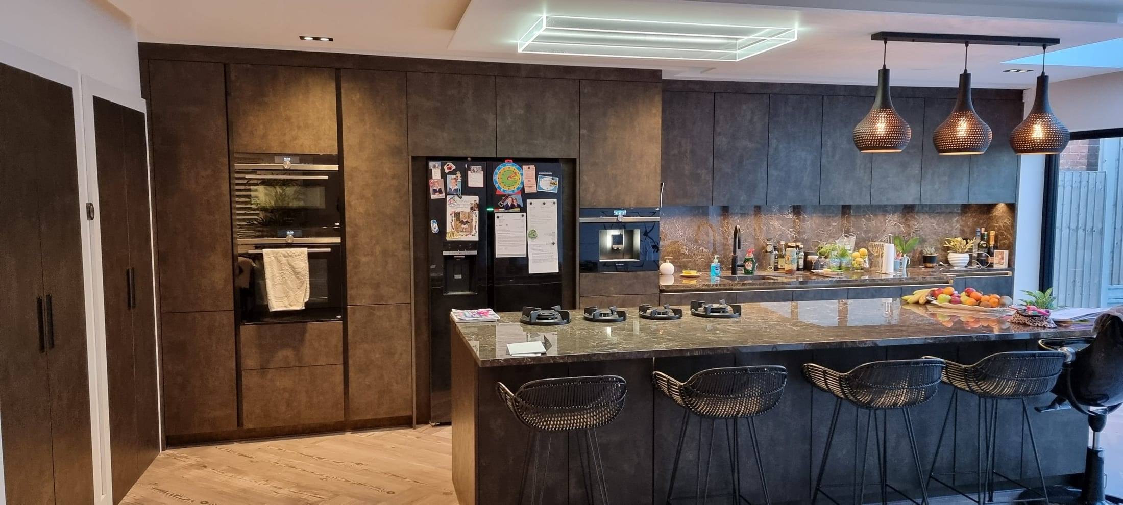 Handleless fitted kitchen in a dark bronze-effect finish with tall units, integrated appliances and a long breakfast island