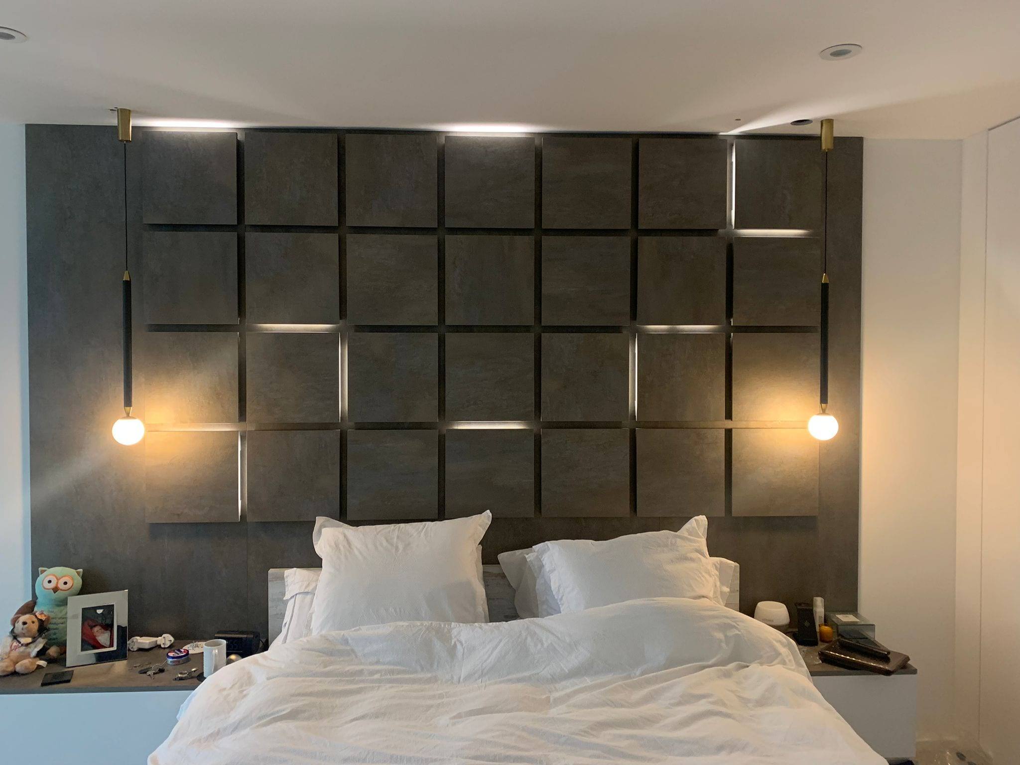 Bespoke headboard wall made of raised square panels with concealed LED lighting and brass pendant lights