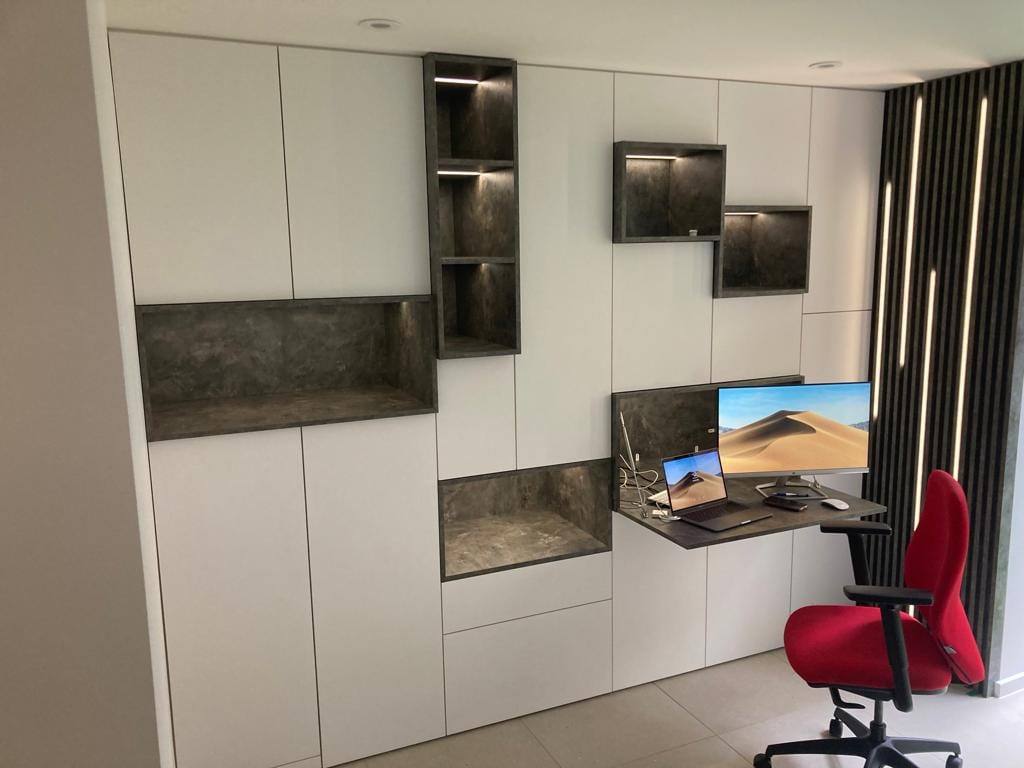 Fitted home office wall with handleless storage, lit display niches and a wall-mounted fold-down desk