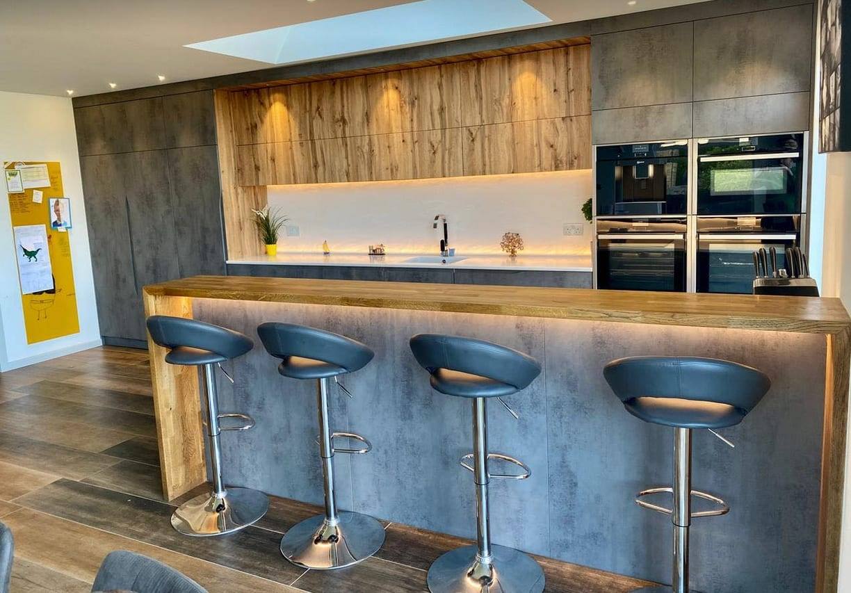 Custom kitchen with concrete-effect doors, rustic oak wall units, under-cabinet lighting and a solid oak breakfast bar