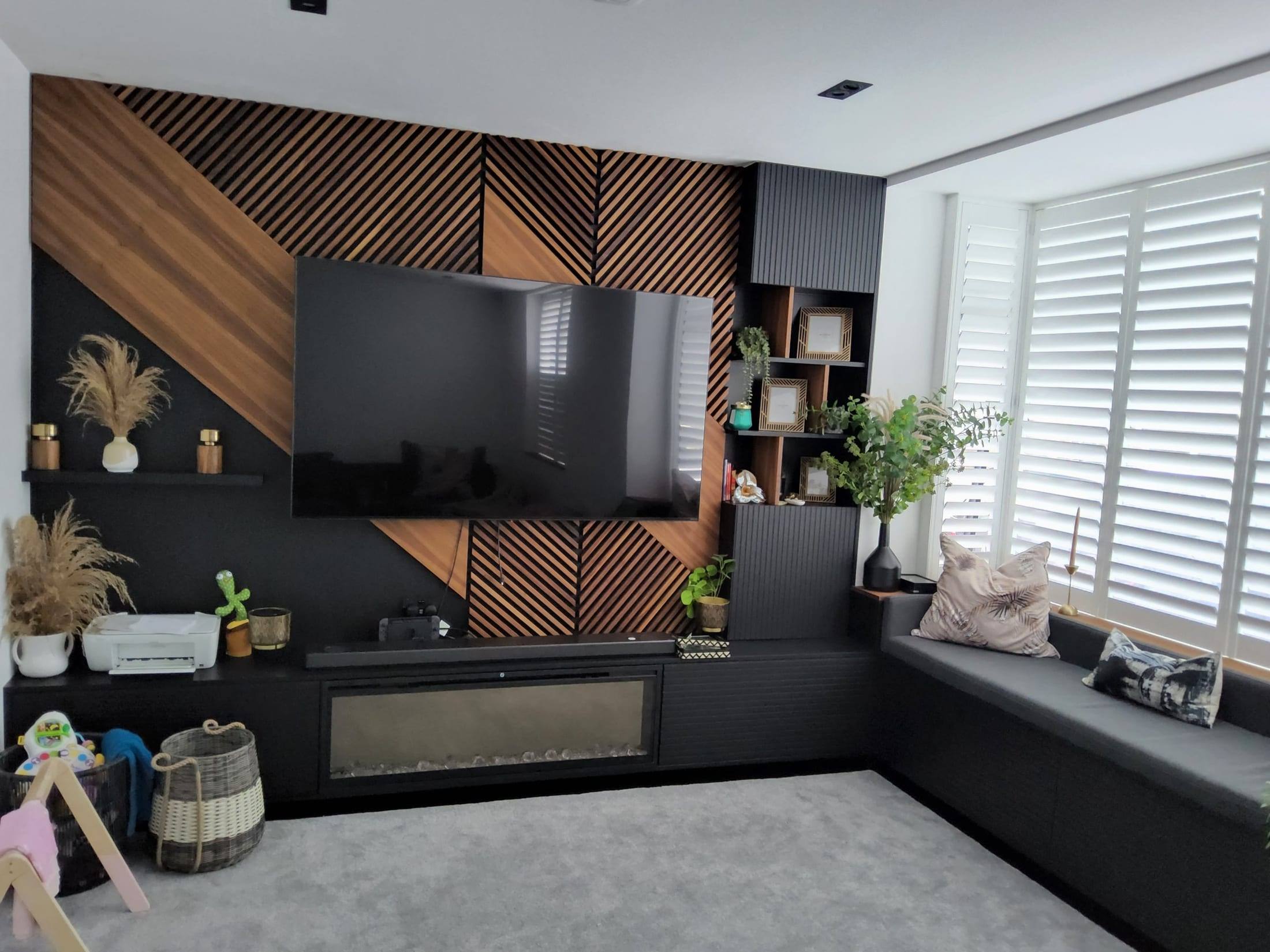 Living room with a diagonal walnut slat TV wall, black fitted media unit with fireplace, shelving and a built-in window seat
