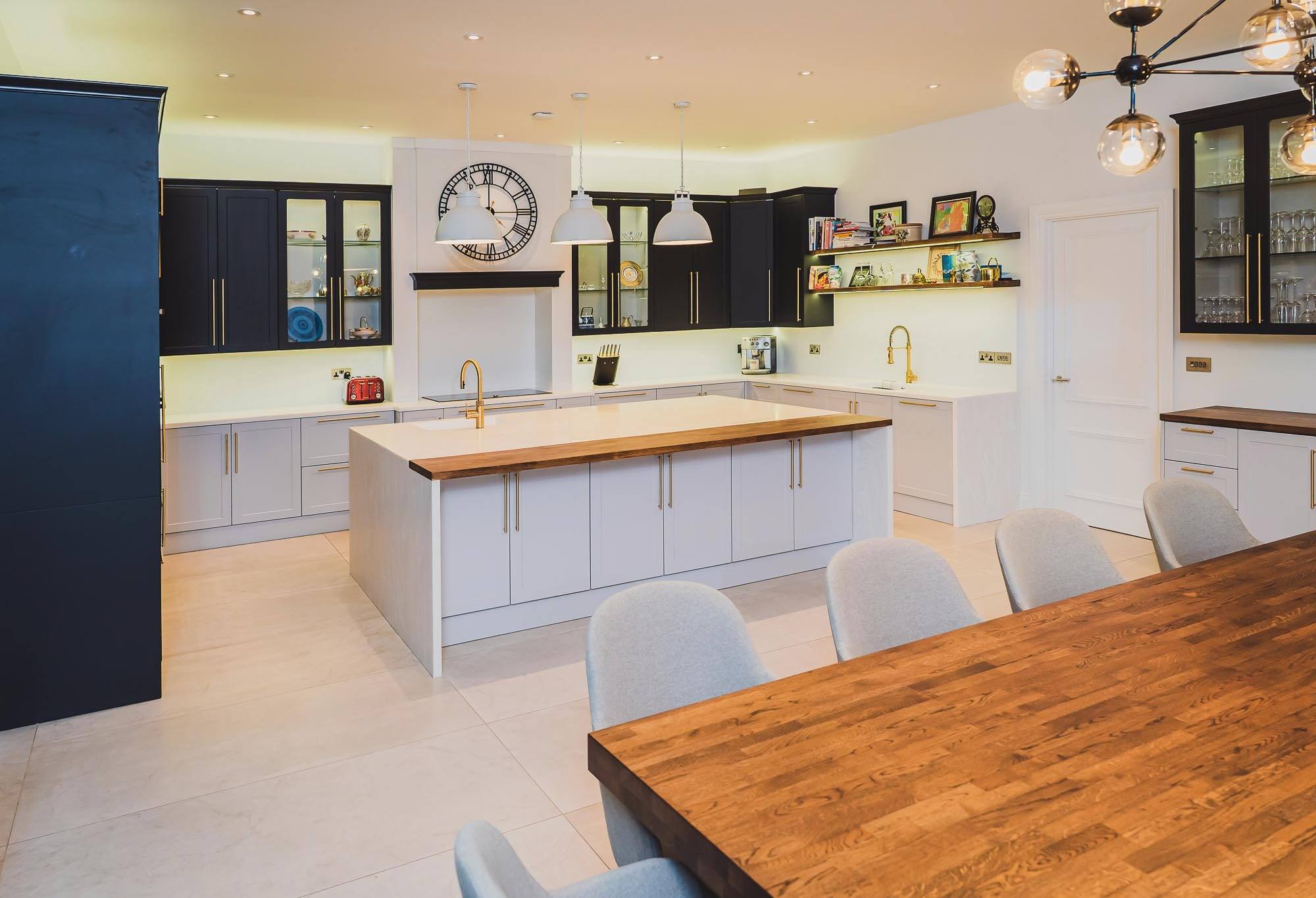 Bespoke shaker kitchen with dark painted wall cabinets, light grey base units, brass handles and an island with an oak breakfast top